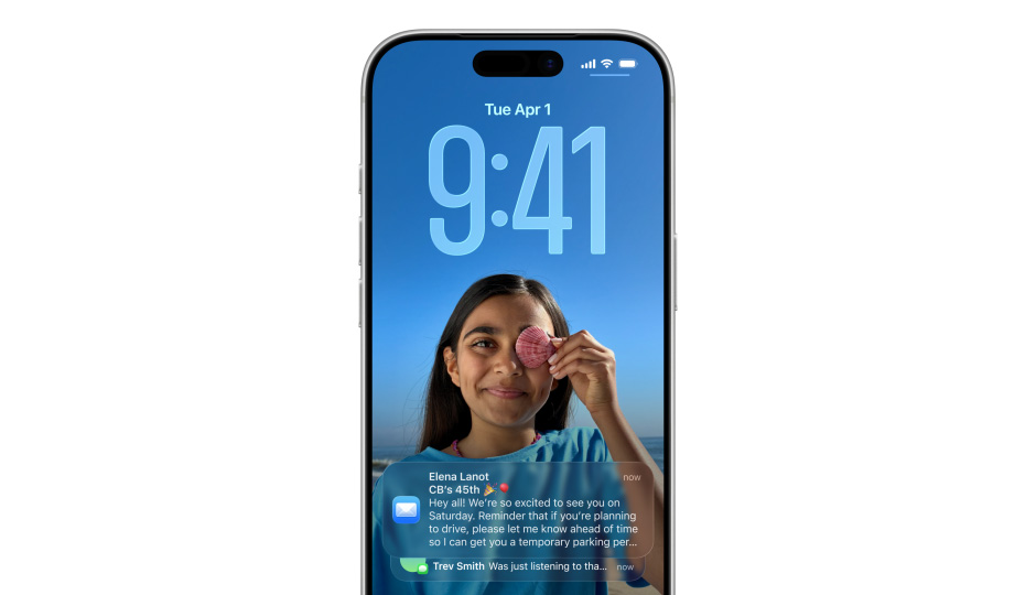L’écran verrouillé d’un iPhone montre une photo, les chiffres de l’heure en Liquid Glass, deux notifications apparaissent au bas de l’écran